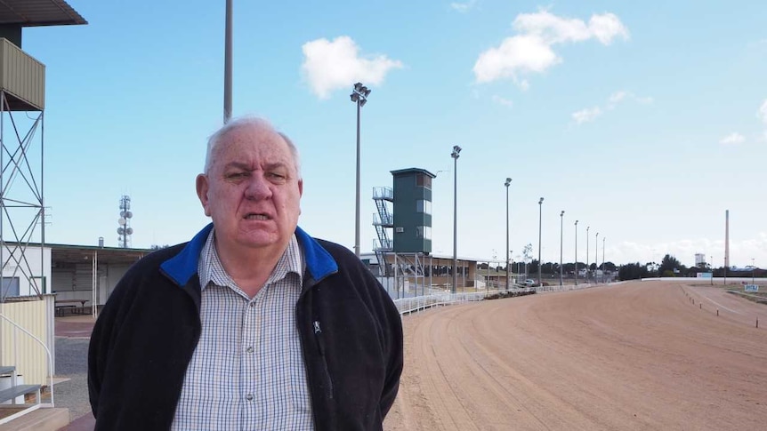 Caucasian male standing on dirt trotting track with towers and lights in the background