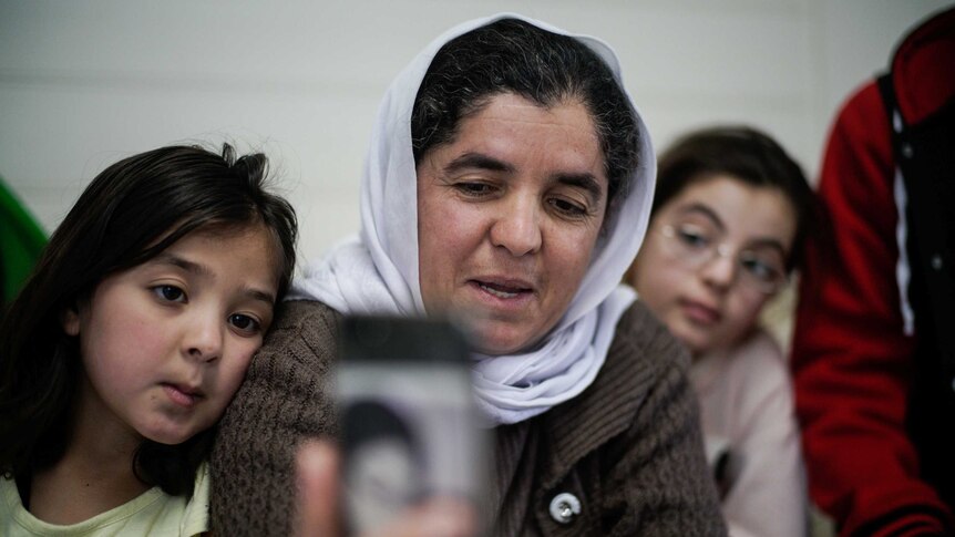 A women and two children look at a phone.