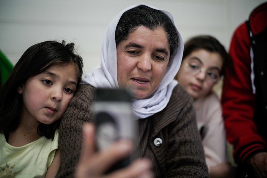 A women and two children look at a phone.