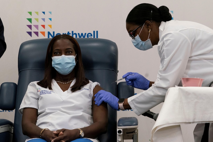 nurse sandra lindsay sits in a blue chair while another nurse wearing blue gloves holds a needle up to her arm