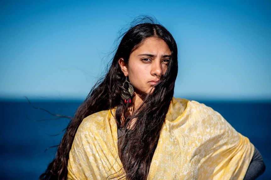 On a bright day near Clovelly beach, you see a woman of Indian descent wearing a yellow scarf.