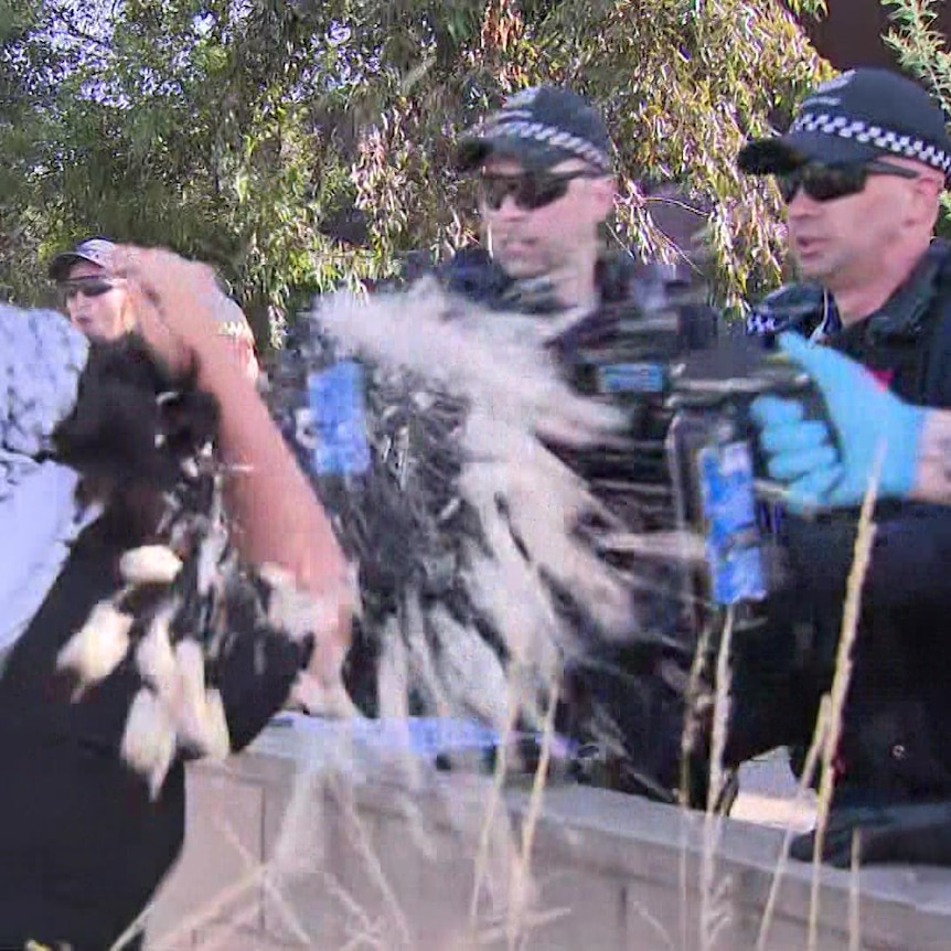 A person covering their face as a liquid is sprayed towards them by several police officers.