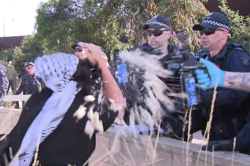 A person covering their face as a liquid is sprayed towards them by several police officers.