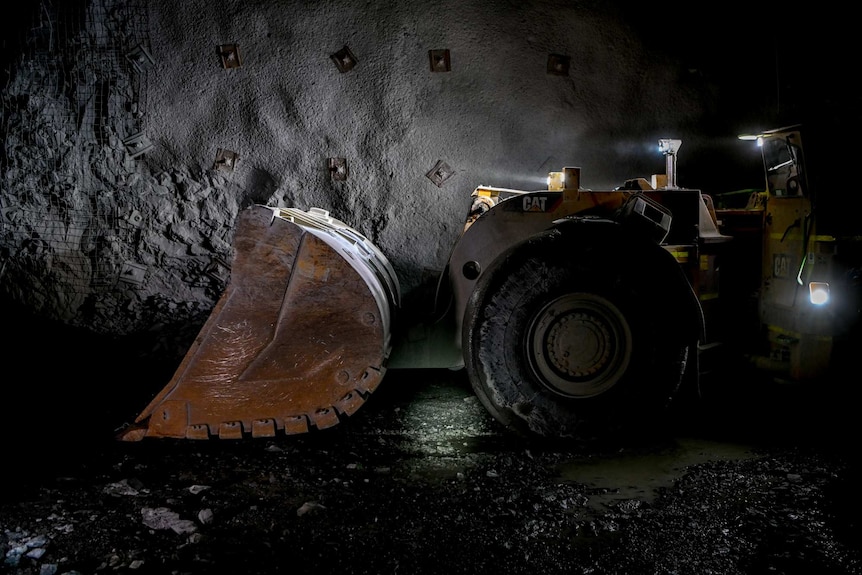 A digger, with spotlights on it, attacks the mine underground.