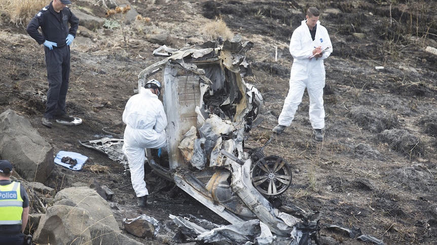 Police look over the burnt out remains of the vehicle, surrounded by scorched earth.