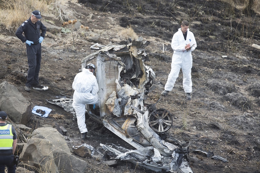 Police look over the burnt out remains of the vehicle, surrounded by scorched earth.