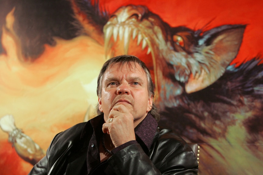 A man stands in front of a poster of a fire-breathing dragon with his hand on his chin.