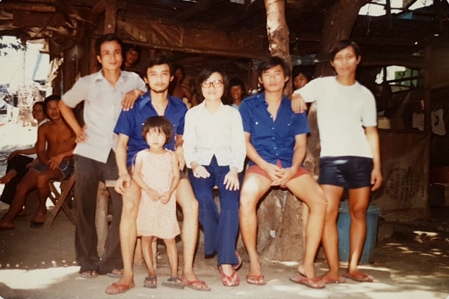 Vietnamese refugees including four men, a woman and a young girl sit in a large shelter in a refugee camp in 1981.