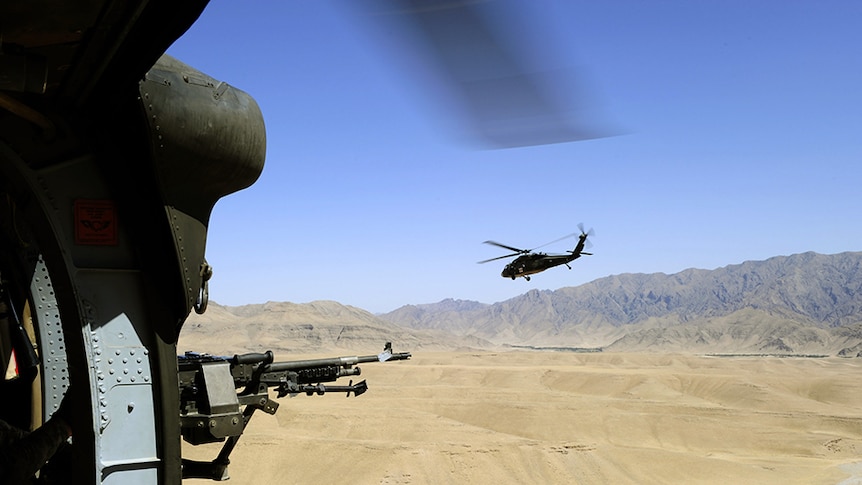 View of out of a helicopter, with gun in foreground, second helicopter and mountain range in distance