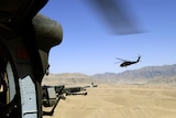 View of out of a helicopter, with gun in foreground, second helicopter and mountain range in distance