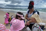 A teacher shows some kids a bug on the beach.