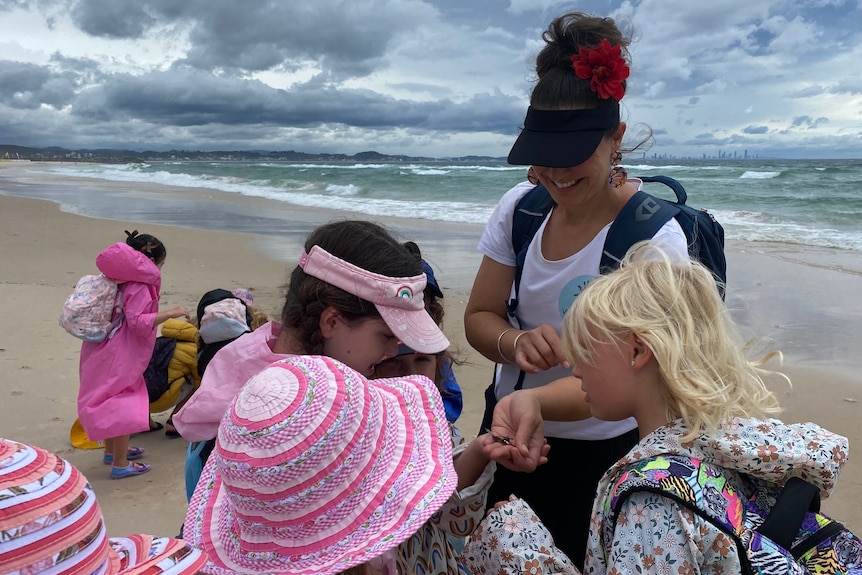 A teacher shows some kids a bug on the beach.