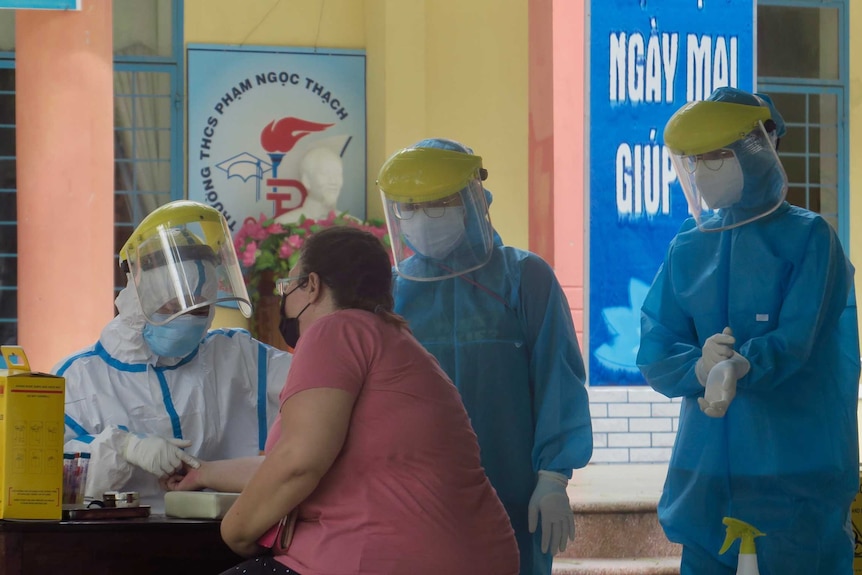 A foreigner takes a coronavirus test in Son Tra District, Da Nang, surrounded by three medical workers in hazmat suits.
