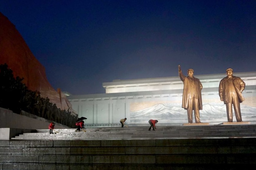 Volunteer children come out to clean around Kim dynasty statues in the rain.