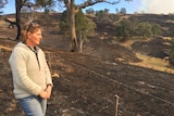 Sharon Walker stands next to a barbed-wire fence, looking at grassland blackened by fire.