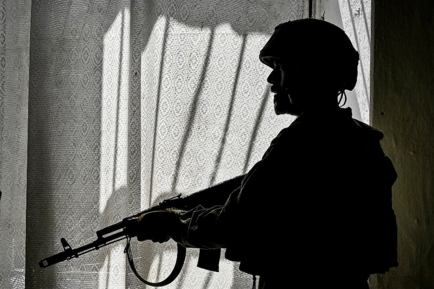 The silhouette of a soldier holding a large gun in the window of a home.