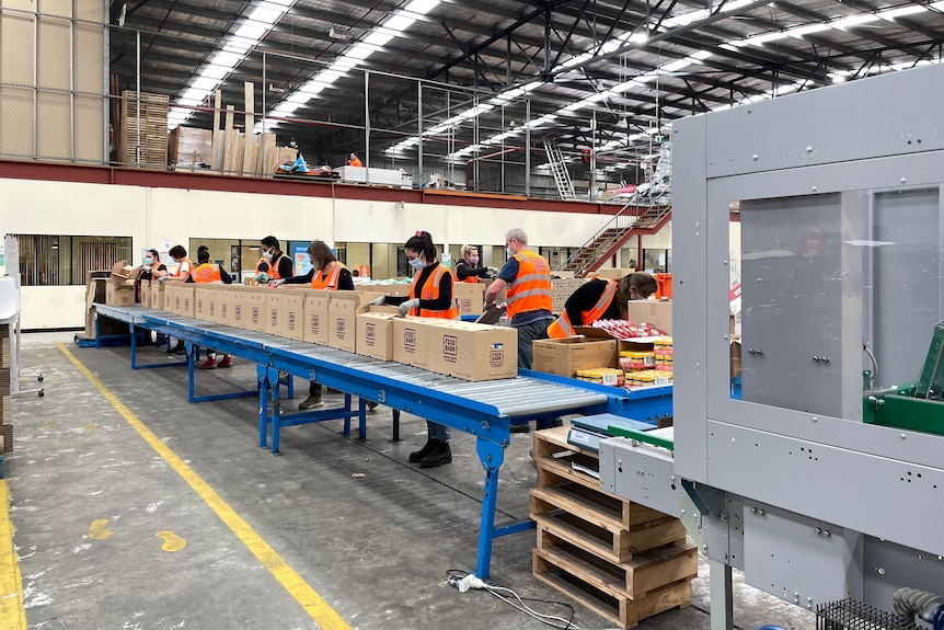 a warehouse with staff packing boxes while standing beside a conveyor belt