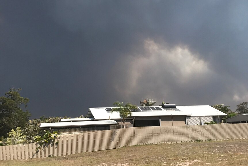 Huge black smoke plume from bushfires looms behind house at Woodgate.