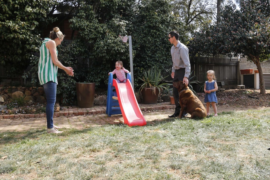 A young family and a pet dog playing in the backyard on their family home