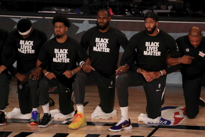 Lakers players, including LeBron James and Anthony Davis, take a knee while arm in arm, wearing a "BLACK LIVES MATTER" shirt