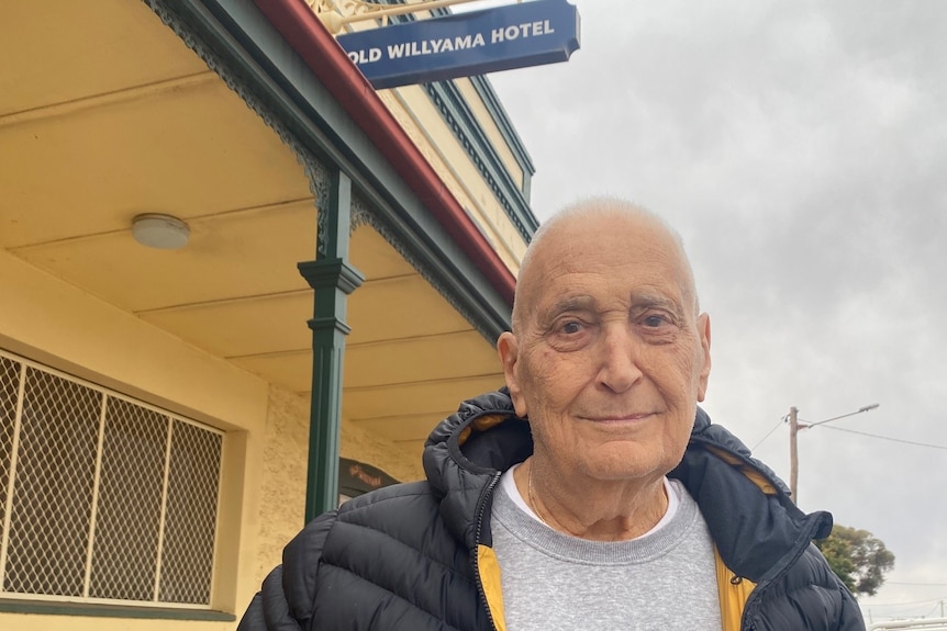 A man smiling lightly at the camera in front of an old hotel building.