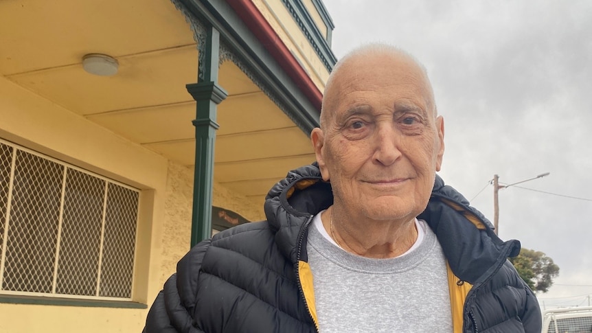 A man smiling lightly at the camera in front of an old hotel building.