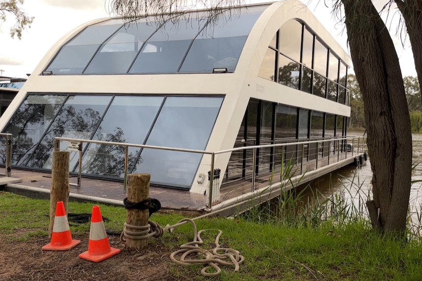 A large houseboat with big paneled windows tied to a post