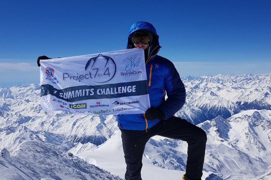 Perth man Steve Plain stands on the summit of Mount Elbrus holding a banner promoting the Seven Summits challenge.