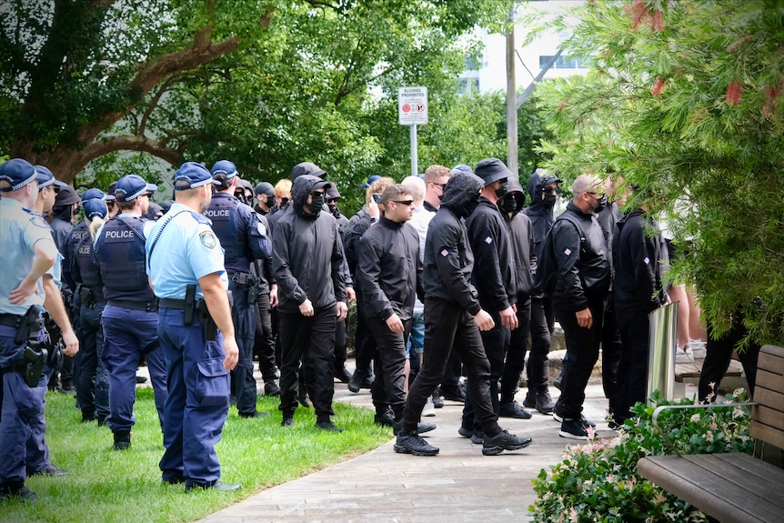 Police monitor a group of men dressed in black