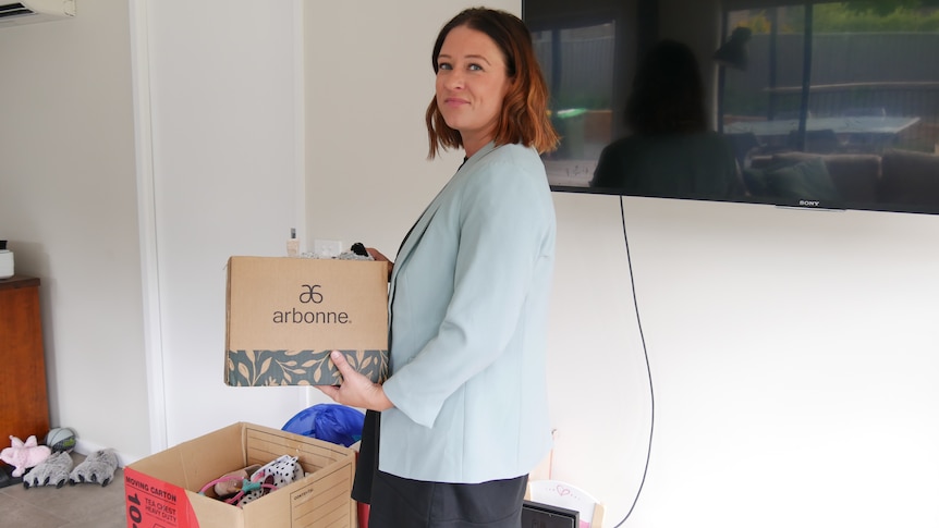 A woman holding a moving box in her new home.