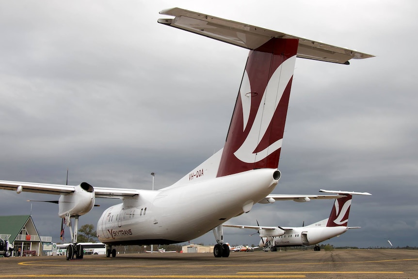 Two planes with maroon livery on tail parked on airport tarmac.