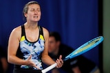 A female tennis player grimaces and gestures with her hands after a point during a match.