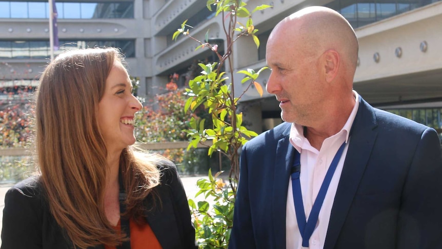 An auburn-haired woman and a bald-headed man laugh in the sunshine.