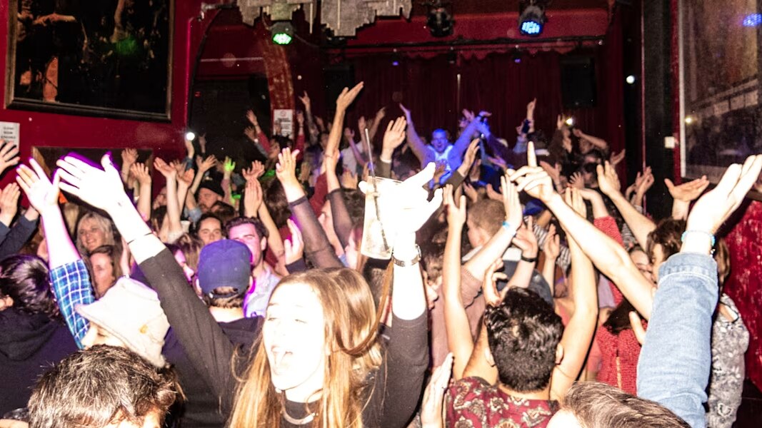 A crowd of people in a nightclub with their hands in the air