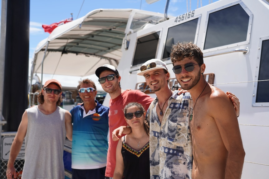 Five young travellers stand infront of boat with experienced sailor Ron Gertler. 