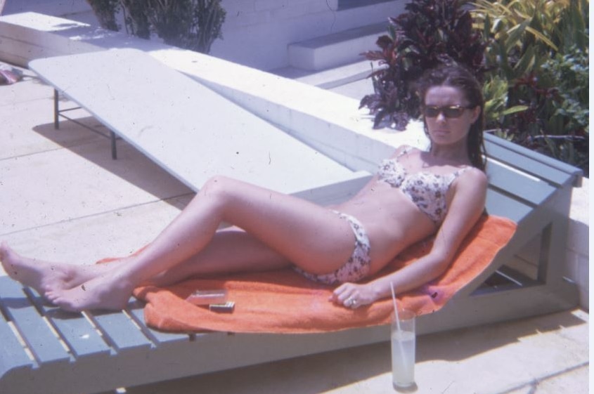 A vintaqe photo of a woman in a bikini sitting on a sun lounge