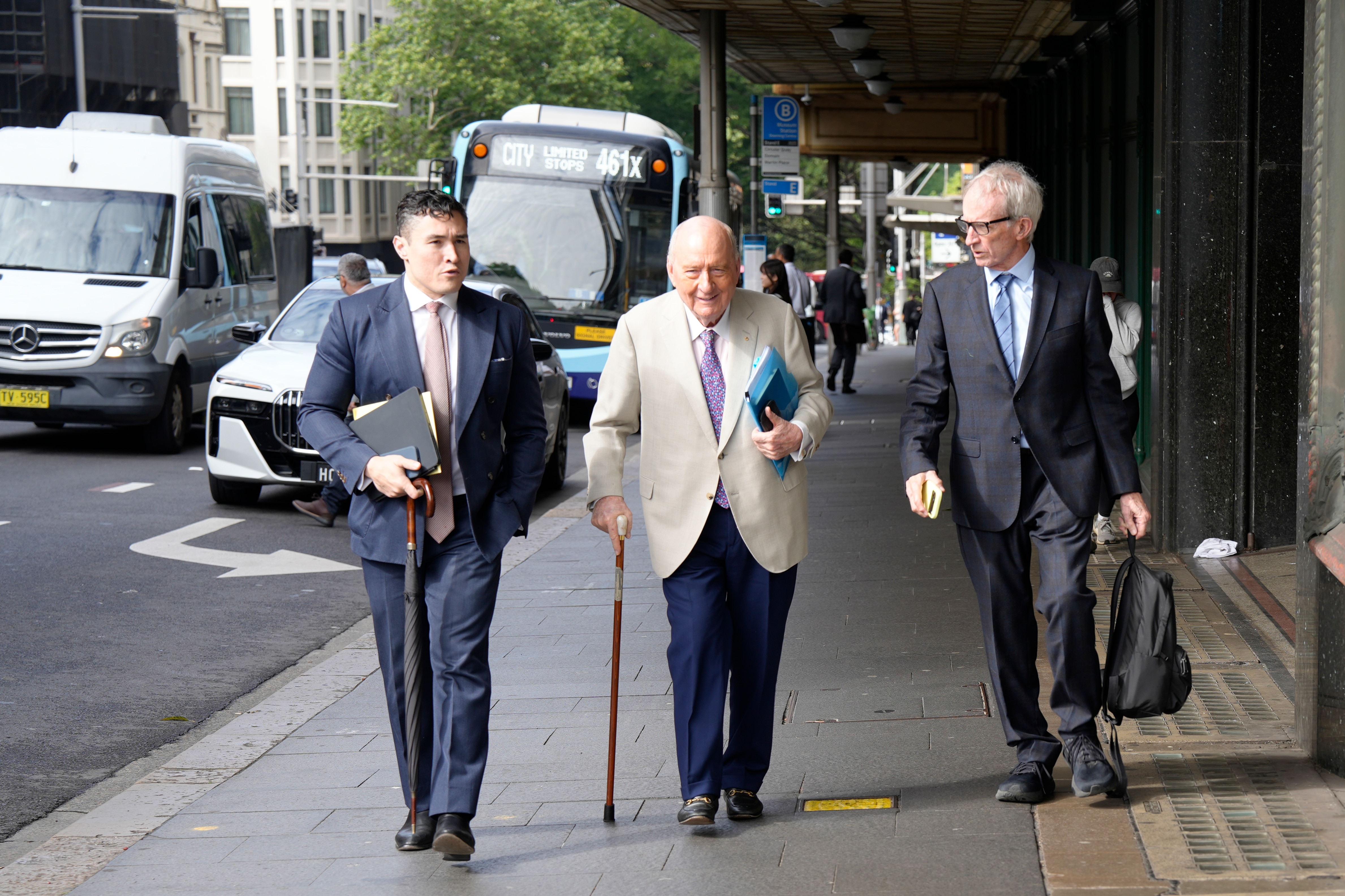 Man in tan coat walks in street with two men in suits