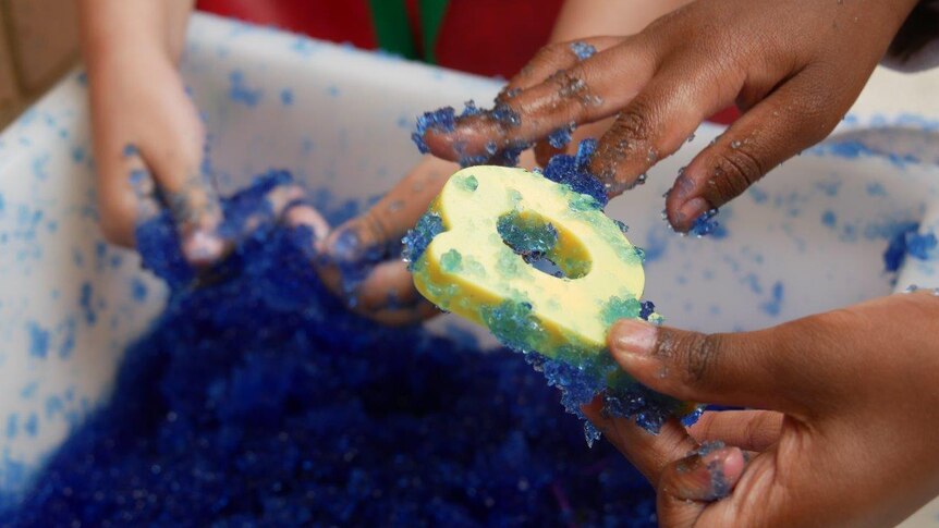A close-up shot showing the hands of young children playing with a blue gel-like substance and giant letters at school.