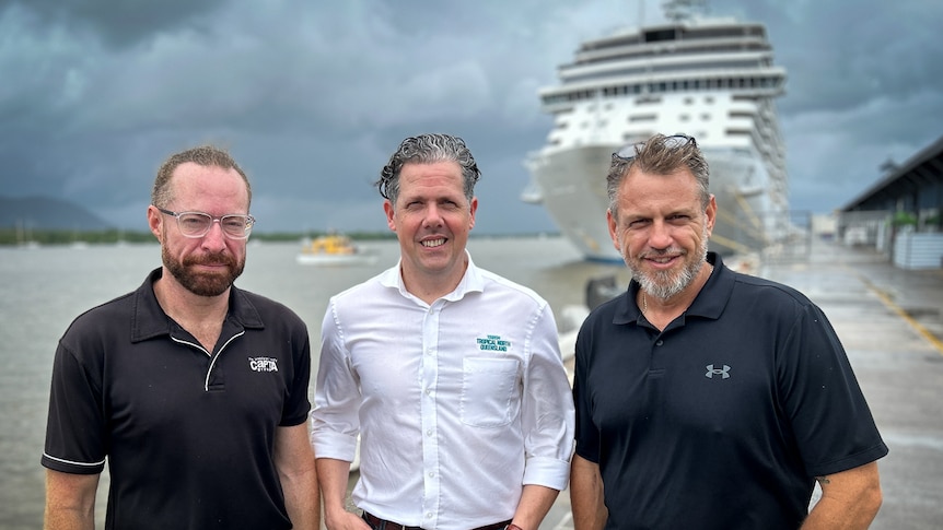 three men standing in front of large cruise ship