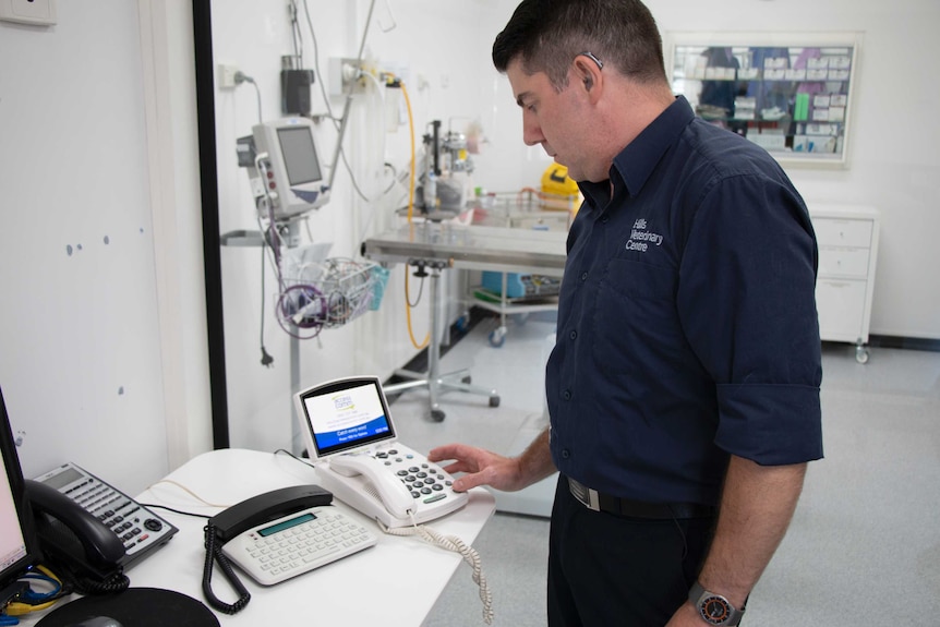 Alex Harrison stands up in his vet clinic and looks over his CapTel phone.