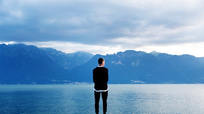 a man in front of mountains looking at a lake