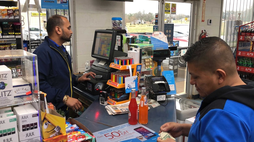 A man sells drinks to another man at a service station in the US.