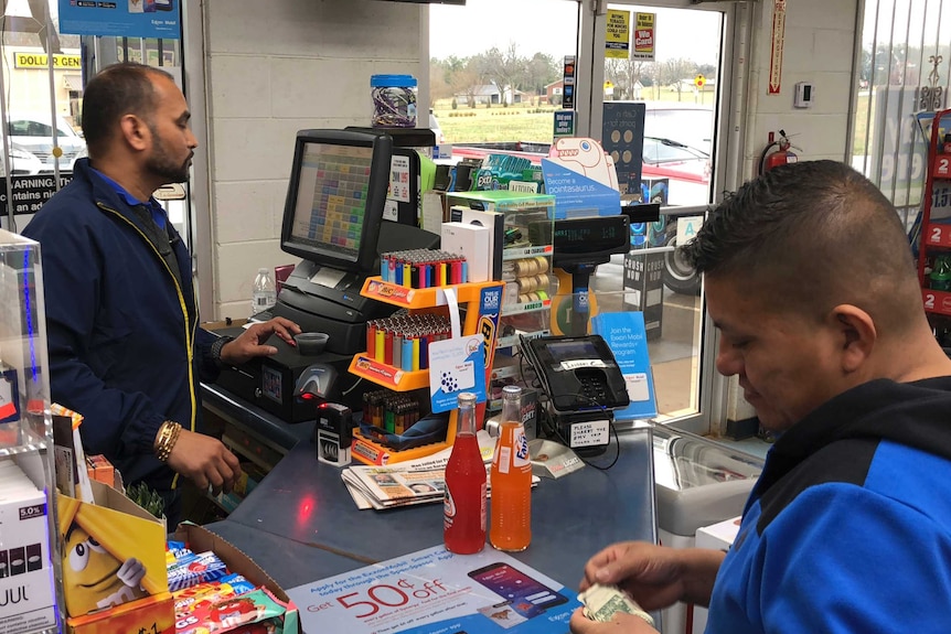 A man sells drinks to another man at a service station in the US.