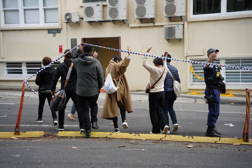 people walking under a police tape with a police officer standing nearby