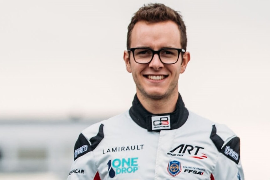 a mean wearing glasses and a white race car driving suit smiles