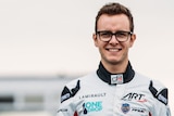 a mean wearing glasses and a white race car driving suit smiles