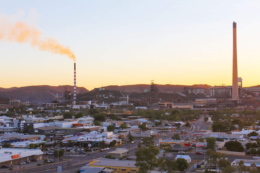 An outback city in the low light of a clear day. Its skyline is dominated by industrial chimneys.