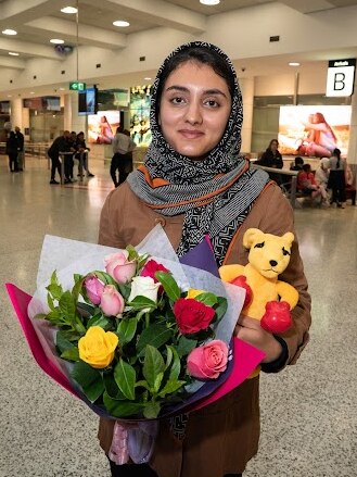 A woman in a headscarf hold a bouquet of flowers and a boxing kangaroo toy 