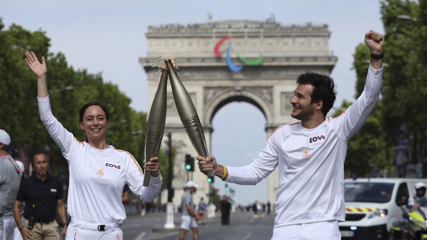 A man and woman dressed in white hold two large torches in Paris