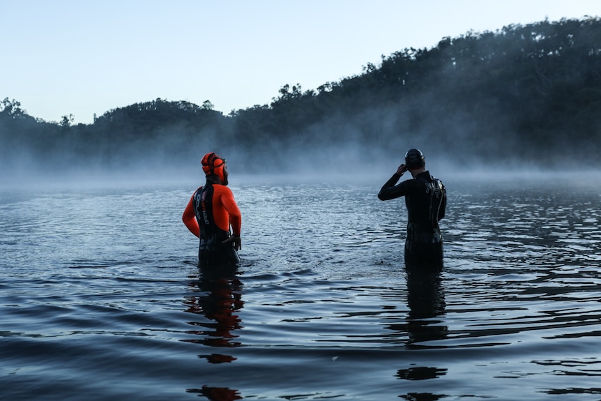 Jessie and Frog in their full length wetsuits standing in the water with their backs to the camera.
